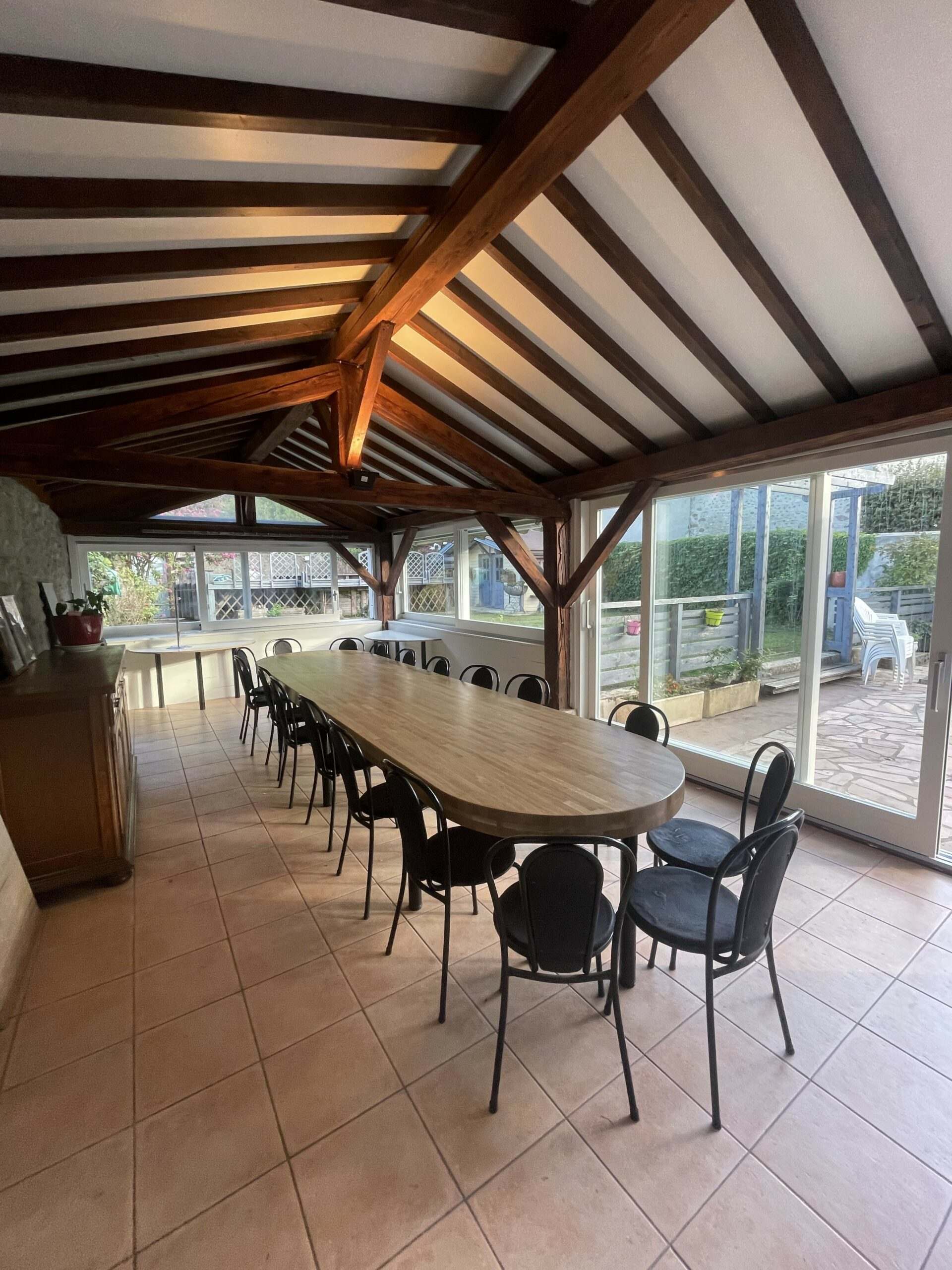 Véranda sous charpente en bois avec une grande table