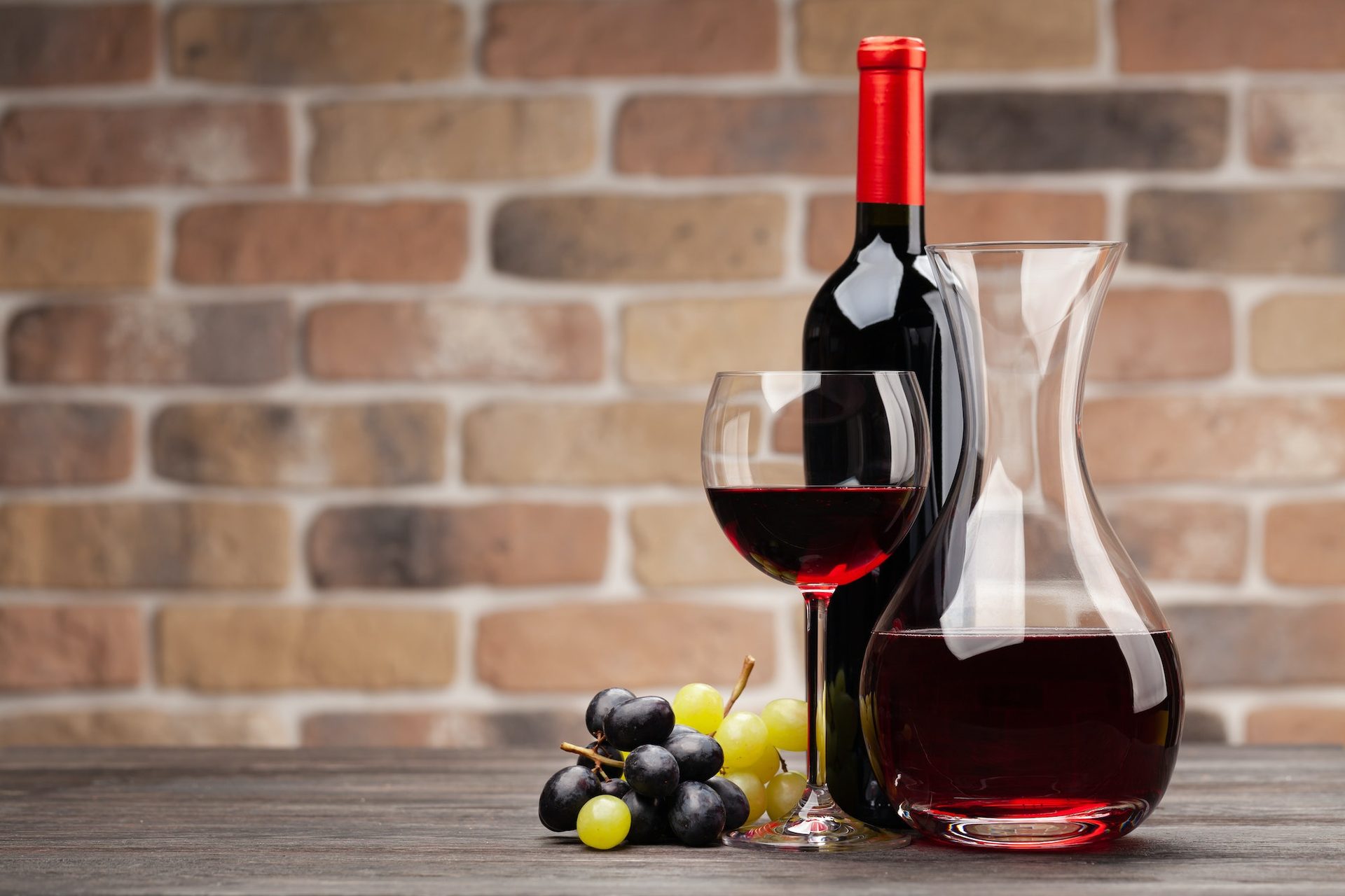 Bouteille, carafe et verre de vin rouge devant un mur de briques